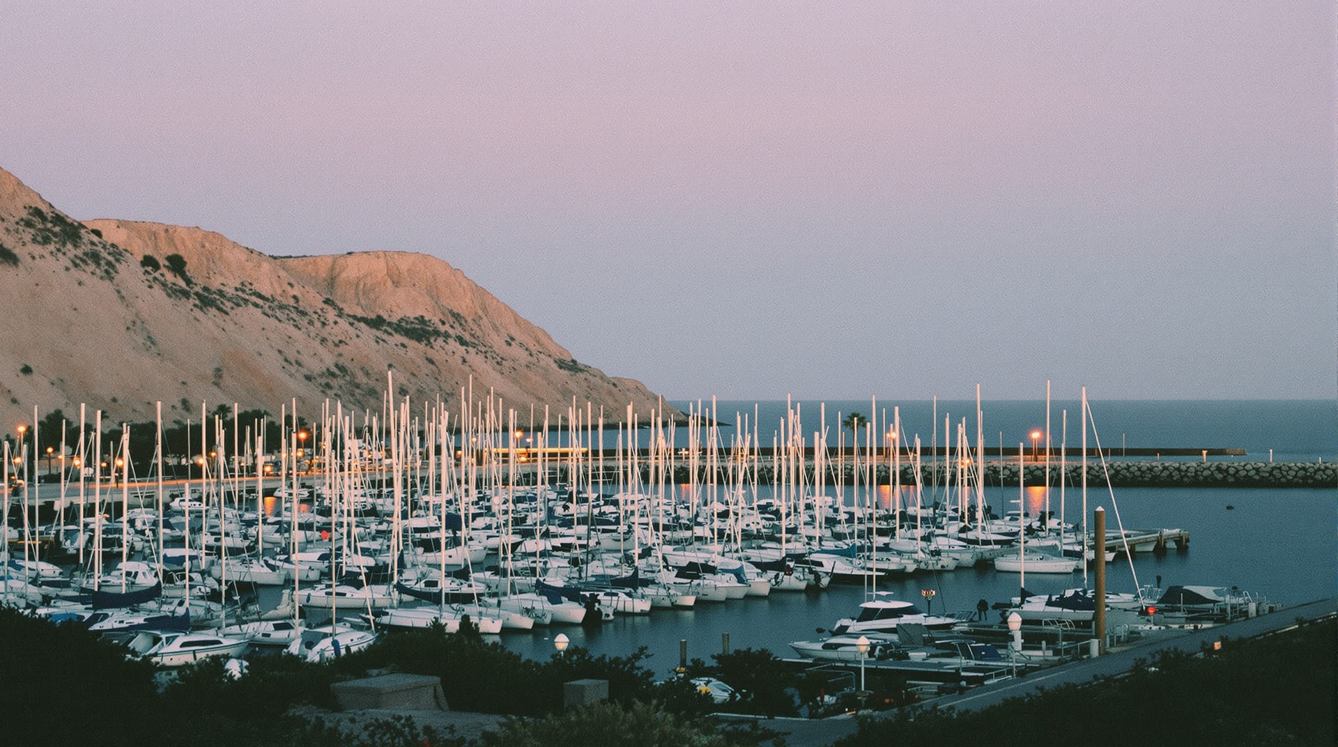 Sailboat masts and a breakwater jetty in a Southern California harbour at dusk